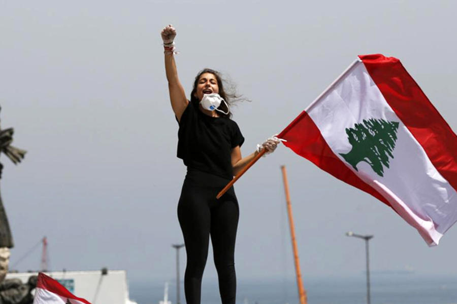 Una manifestante se encuentra en la parte superior de su automóvil gritando consignas y ondeando la bandera libanesa, durante una protesta por las calles para expresar el rechazo del liderazgo político al que culpan por la crisis económica y financiera, en Beirut, Líbano, miércoles, abril. 22, 2020.