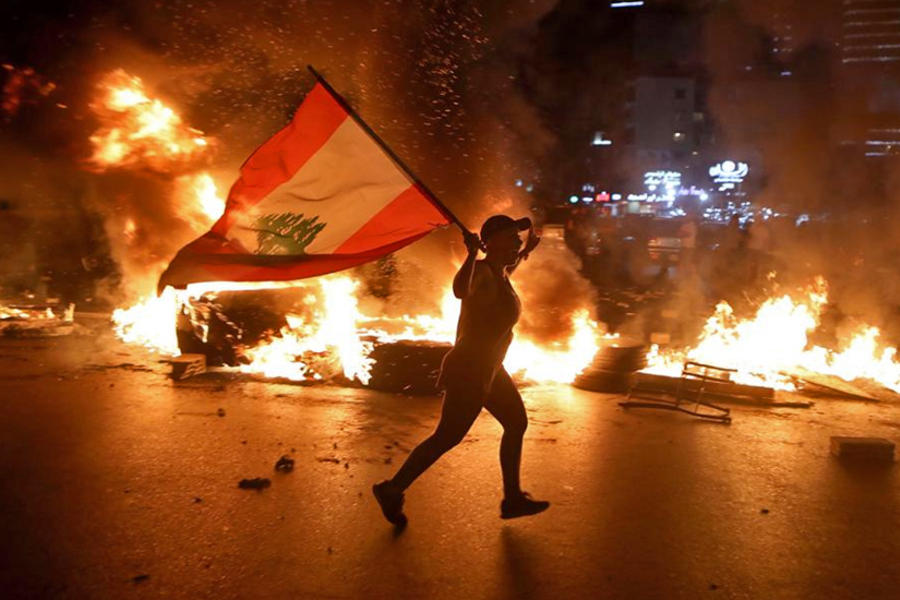Un manifestante con la bandera libanesa corre mientras bloquean la carretera Jounieh-Trípoli con neumáticos en llamas, Beirut, 11 de junio de 2020.