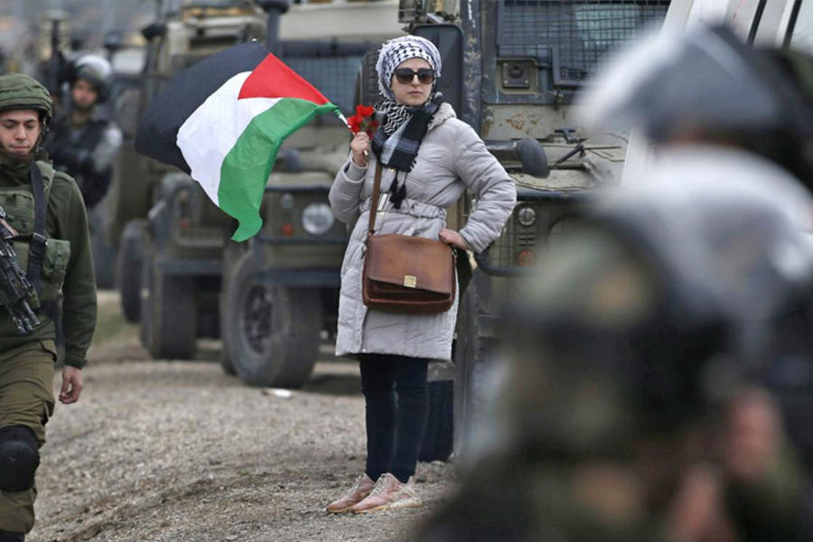 Una mujer palestina con la bandera nacional se encuentra junto a los soldados israelíes durante una manifestación contra los asentamientos israelíes en la aldea de Qusra, en la Cisjordania ocupada por Israel el 2 de marzo (AFP)