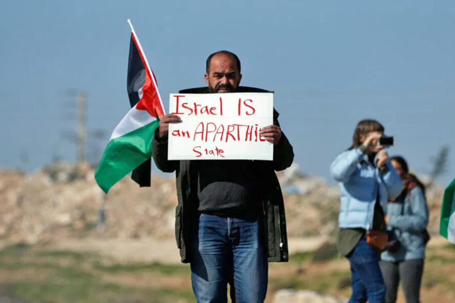Palestino lleva un cartel que dice "Israel es un estado de apartheid", Cisjordania ocupada, 2019. Foto: AFP. 