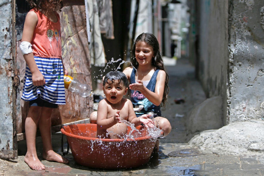 Niños palestinos se refrescan durante una ola de calor en el campo de refugiados de Bureij, en la Franja de Gaza, en mayo de 2020. Foto: AFP.
