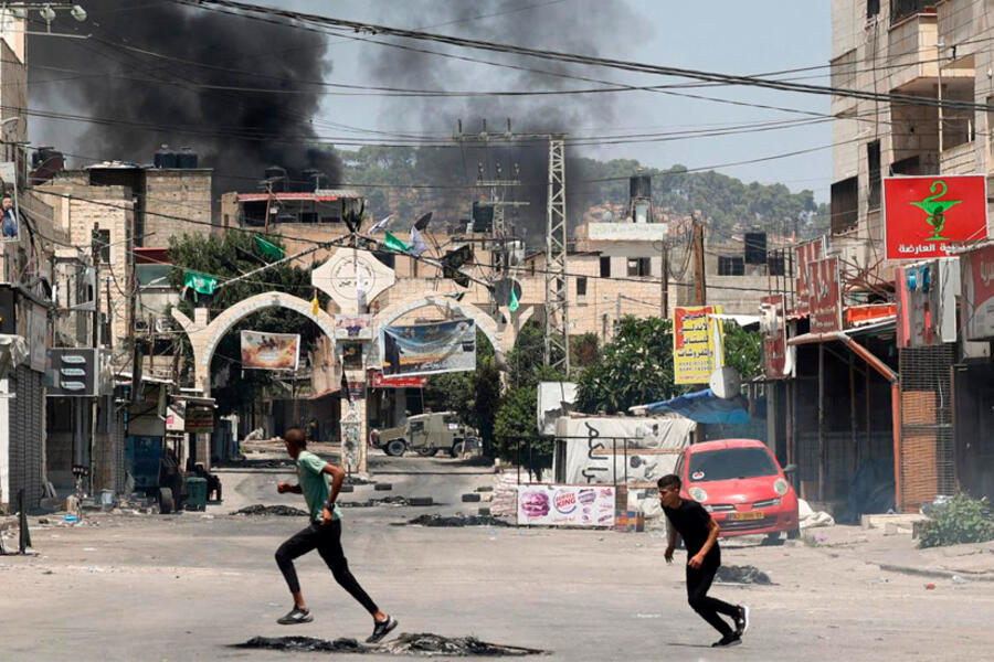Jóvenes palestinos corren a refugiarse cerca de Jenin mientras el humo se eleva en medio de una ofensiva israelí en la ciudad ocupada de Cisjordania | Julio 3, 2023 (Foto: AFP)