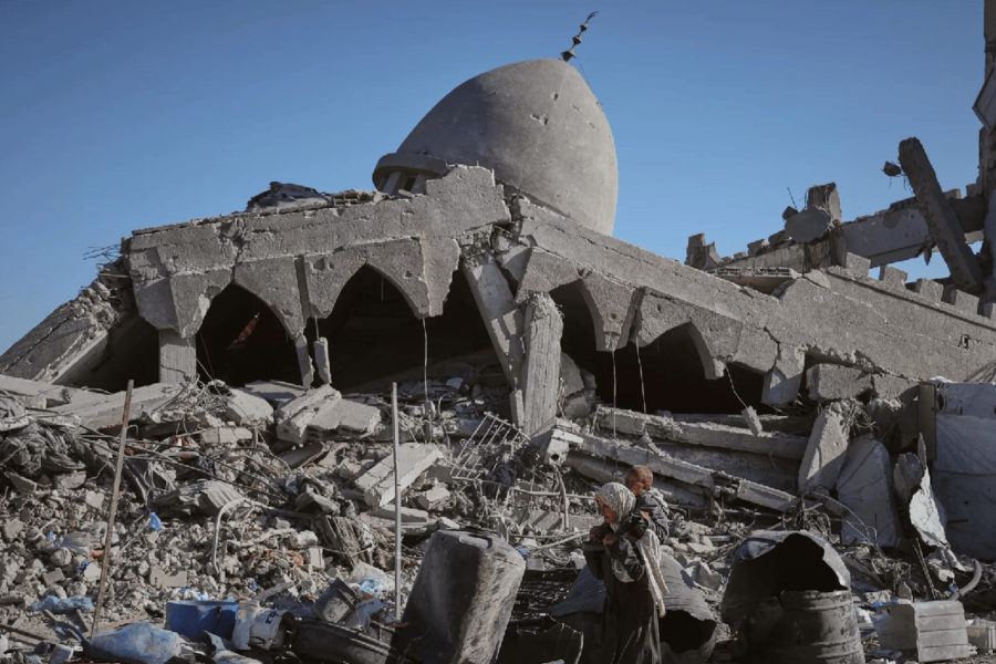 Una mujer palestina pasa cargando a su hijo frente a una mezquita destruida por las bombas israelíes en la ciudad de Gaza | Octubre 26, 2025 (Foto: Jehad Alshrafi / AP)